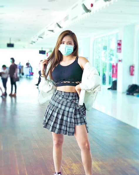 Jeii Pong wearing a black crop top and grey plaid mini shirt and a blue face mask.