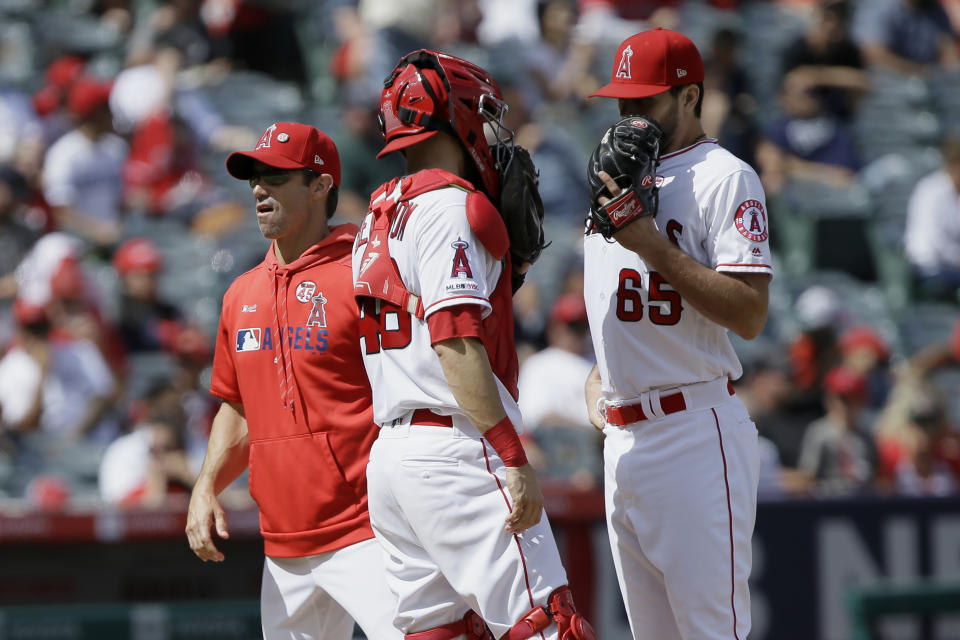 Los Angeles Angels manager Brad Ausmus, left, walks away after switching in relief pitcher Jake Jewell, right, who talks with catcher Anthony Bemboom, center, during the fourth inning of a baseball game against the Houston Astros in Anaheim, Calif., Sunday, Sept. 29, 2019. (AP Photo/Alex Gallardo)