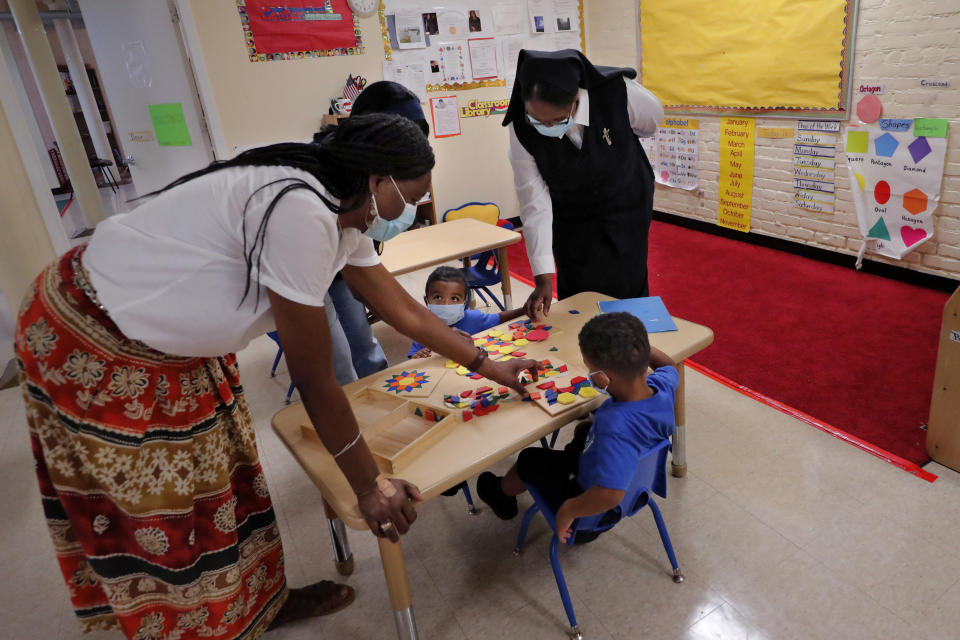 Sister Andria Donald of the Sisters of the Holy Family works with teachers Janice Donalds, left, and Robin Jackson, partially visible, along with children Julio Washington, right, and Santana Washington, at the St. John Berchmans Early Childhood Care Center in New Orleans, Thursday, July 23, 2020. In the archdioceses of New Orleans and Chicago, top leaders are encouraging their schools to place a new emphasis on teaching about racial justice, as well as the history of Black Catholics. (AP Photo/Gerald Herbert)