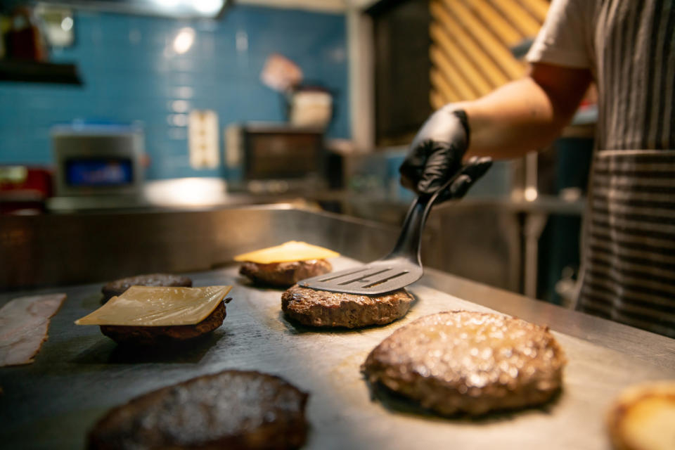 Burgers on a griddle being cooked, some with cheese on top