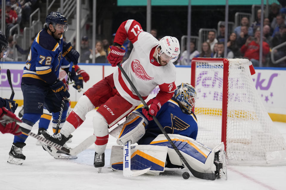 Detroit Red Wings' Michael Rasmussen (27) reaches for a loose puck as St. Louis Blues goaltender Jordan Binnington and Justin Faulk (72) defend during the third period of an NHL hockey game Tuesday, Dec. 12, 2023, in St. Louis. (AP Photo/Jeff Roberson)