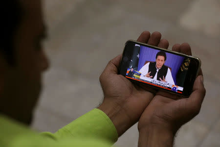 A journalist poses with a cell phone displaying Imran Khan, Prime Minister of Pakistan, speaking to the nation in his first televised address, in Karachi, Pakistan August 19, 2018. REUTERS/Akhtar Soomro