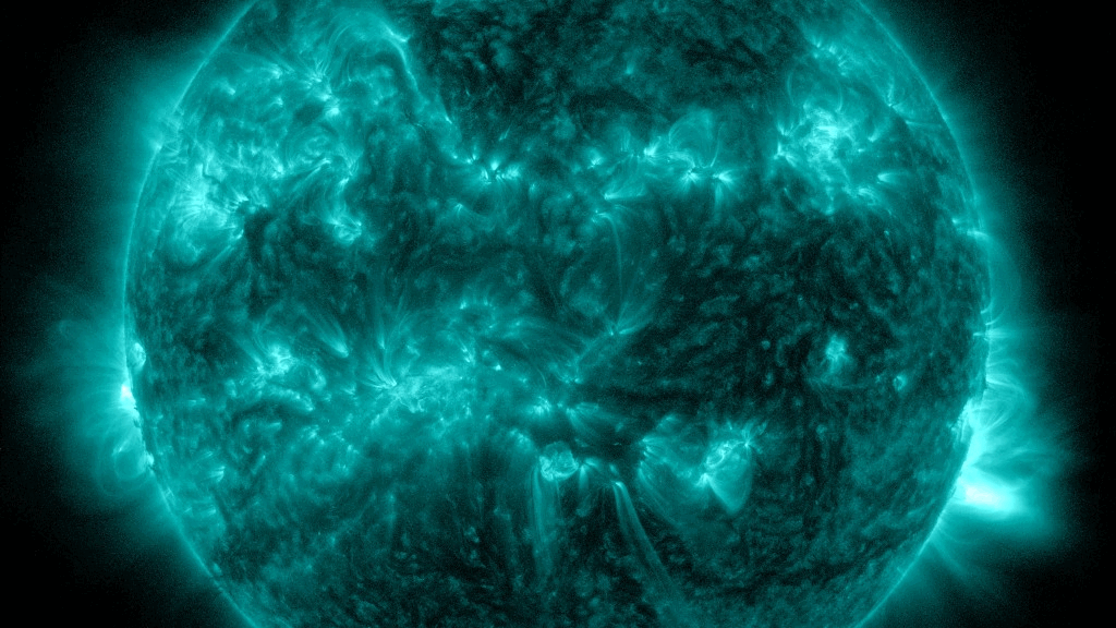  A false color image of the sun, shown in blue greens, as flares a swirls erupt from its surface. 