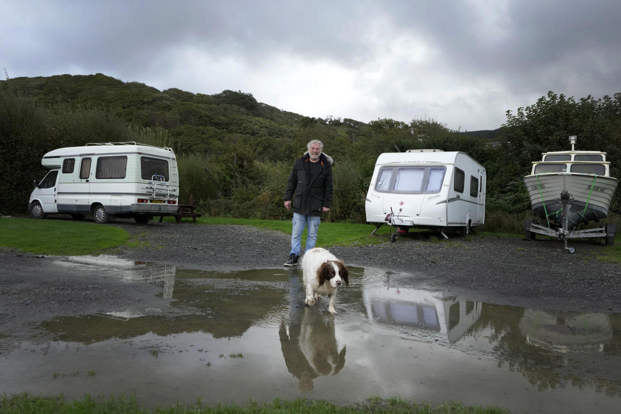 Stuart Eves a Fairbourne resident walks with his dog Lucy in Fairbourne village in Gwynedd in Wales, Wednesday, Oct. 20, 2021. Like many others who came to Fairbourne, Stuart Eves knew this coastal village in northern Wales was home for life when he moved here 26 years ago. However, authorities say that by 2054, it would no longer be sustainable to keep up flood defenses there because of faster sea level rises and more frequent and extreme storms caused by climate change. (AP Photo/Kirsty Wigglesworth)