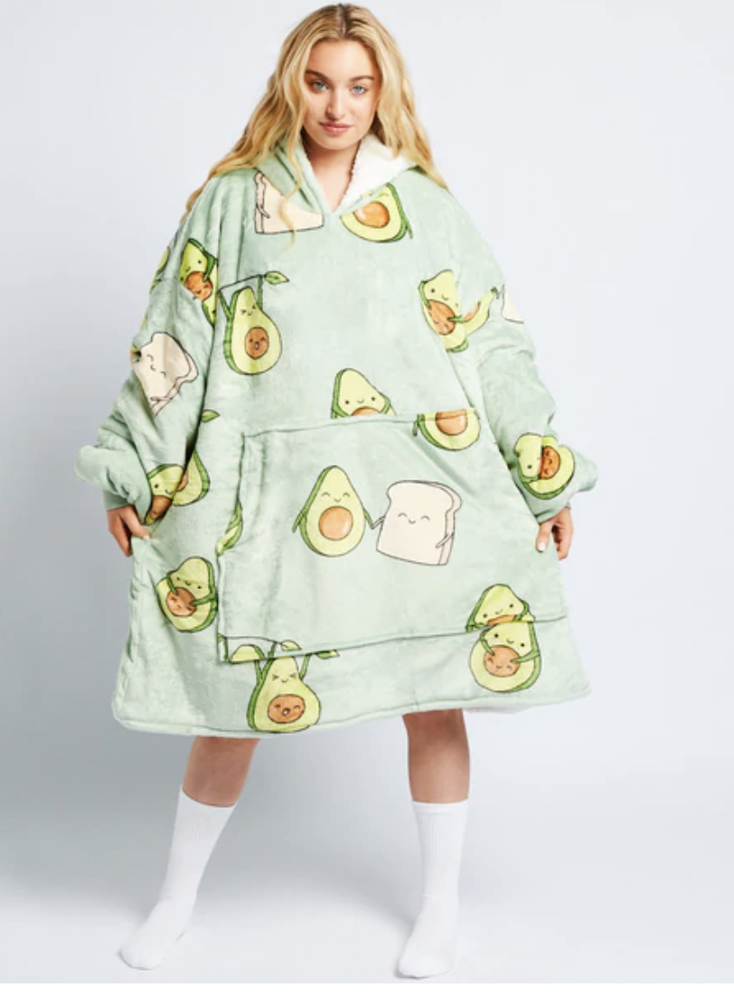 A model with long blonde hair stands wearing a green The Oodie with cartoon images of avocados and toast