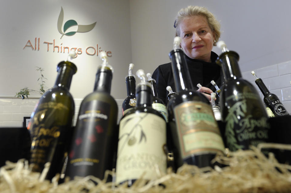 This photo taken Feb. 12, 2014 shows California Olive Oil Council Executive Director Patricia Darragh posing with a collection of California olive oil at the All Things Olive shop in Washington. It's a pressing matter for the tiny U.S olive oil industry. Shoppers are more often pouring European oil _ it's cheaper and viewed as more authentic than the American competition. And that's pitting U.S. producers against importers of the European oil. Some liken the battle to the California wine industry's struggles to gain acceptance decades ago. The tiny California olive industry says European olive oil filling U.S. shelves often is mislabeled and lower grade. They're pushing the federal government to give more scrutiny to imported varieties. One congressman-farmer even goes as far as suggesting labels on imported oil say "extra rancid" rather than extra virgin. Stricter standards might help American producers grab more market share from the dominant Europeans. (AP Photo/Susan Walsh)
