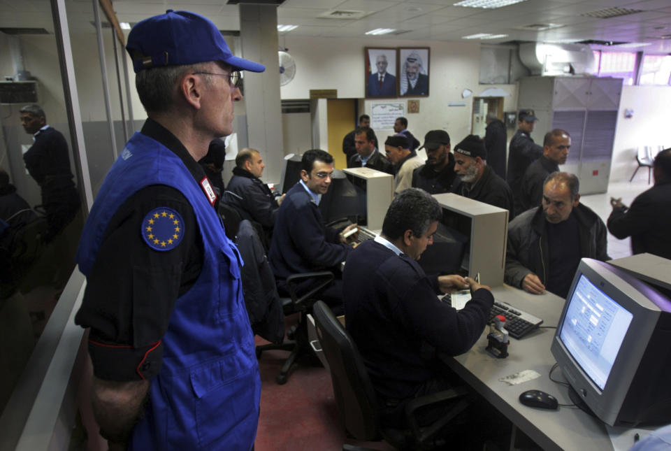 FILE - A European Union monitor watches as Palestinian security officers check the documents of travelers crossing at the Rafah terminal into Egypt, in the southern Gaza Strip, Friday, March 9, 2007. The European Union withdrew the monitoring mission formed to promote a two-state solution between Israel and the Palestinians from Gaza after the Hamas militant group seized power in 2007. But 16 years later, the mission continues to maintain offices in Israel in hopes of one day returning. Critics say the ongoing Western commitment to the two-state solution fails to recognize the changing circumstances in the region and maintains a costly-status quo. (AP Photo/Khalil Hamra, File)