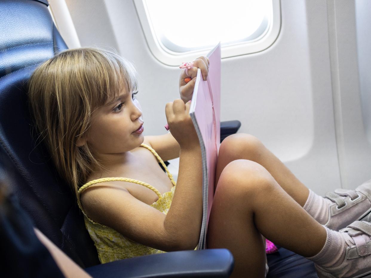 Blonde toddler girl sitting on airplane seat painting in coloring book