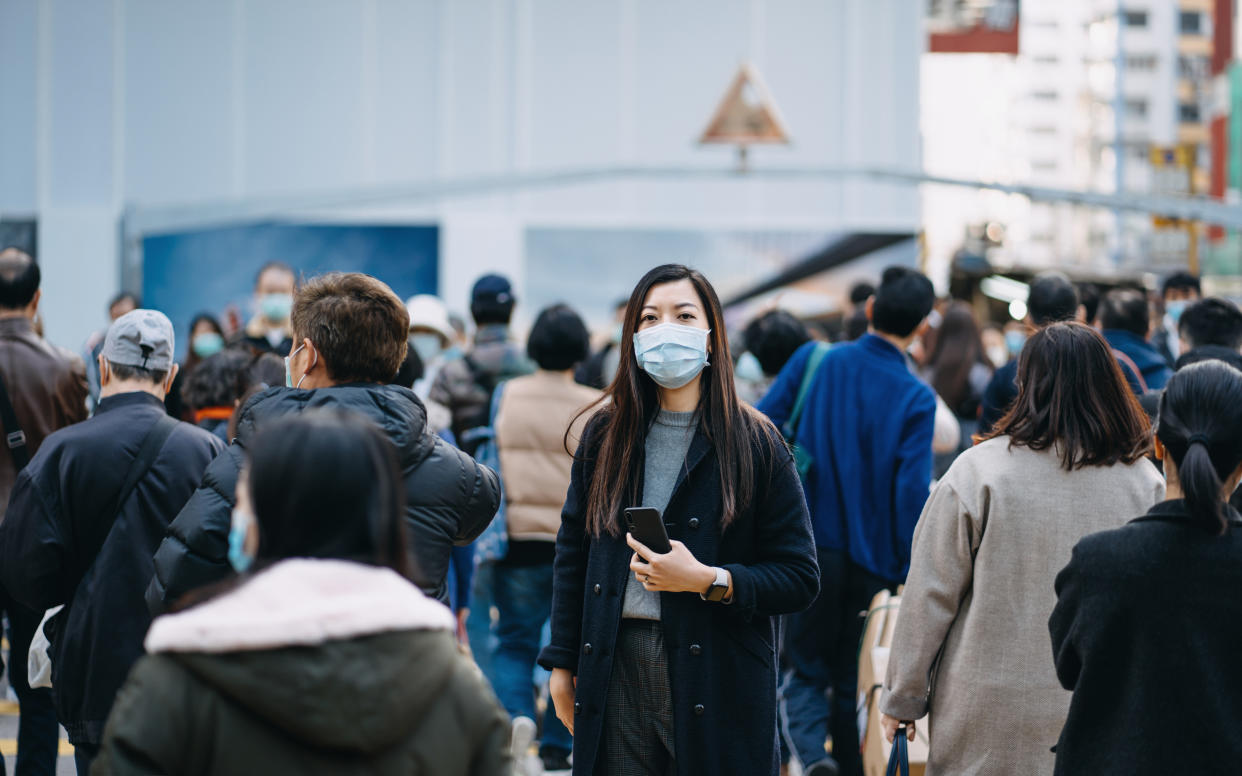 Woman with COVID-19 face mask amid pedestrians passing by. 