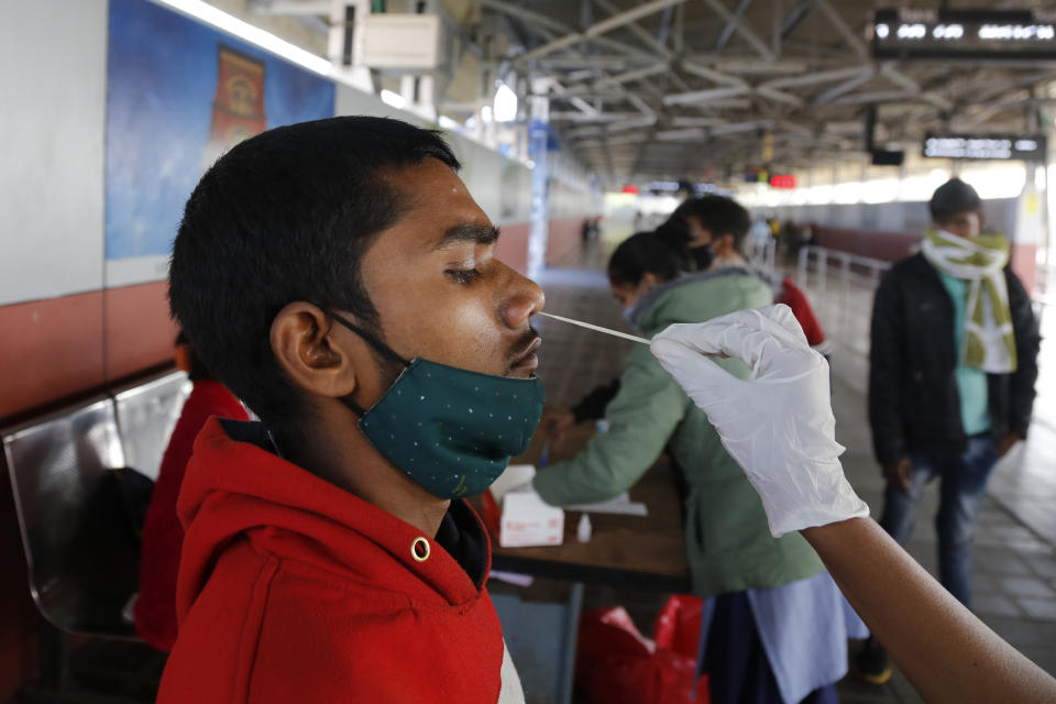 A health worker takes a swab sample of a passenger entering the city to test for COVID-19 at a railway station in Ahmedabad, India, Friday, Dec. 3, 2021. India on Thursday confirmed its first cases of the omicron coronavirus variant in two people and officials said one arrived from South Africa and the other had no travel history. A top medical expert urged people to get vaccinated. (AP Photo/Ajit Solanki)