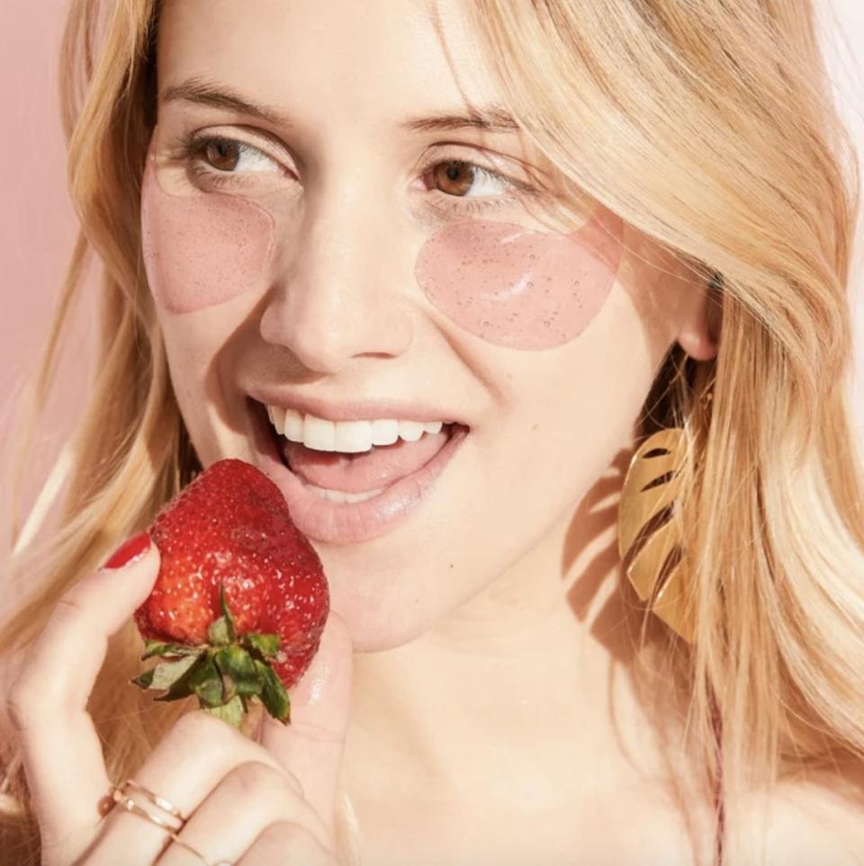 Woman with under-eye patches holds a strawberry near her mouth