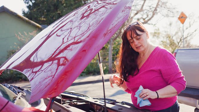 A mature 55+ woman checks under the hood of her car.