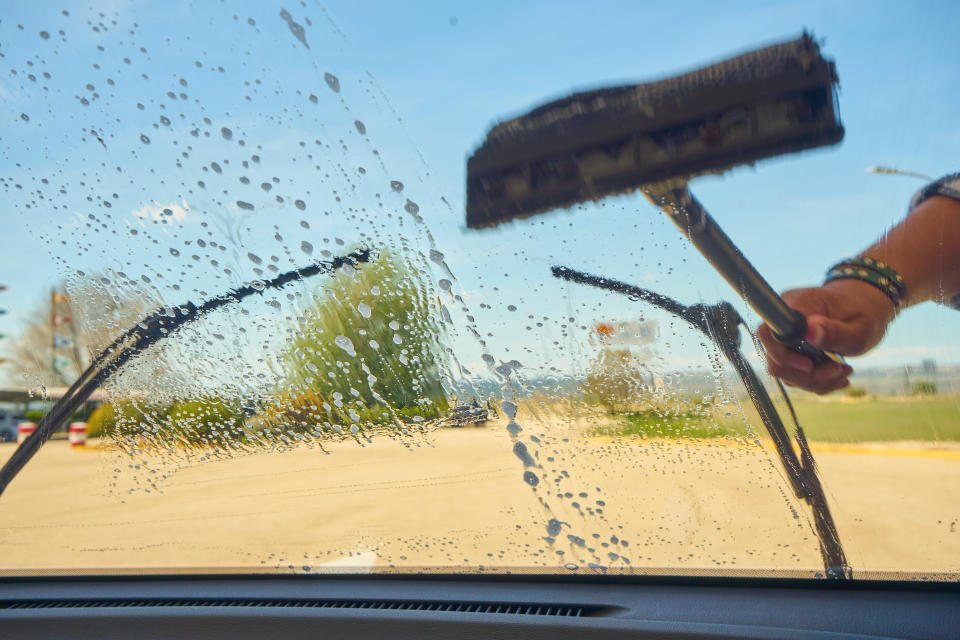 Washing a car's windscreen from the outside on a sunny day.