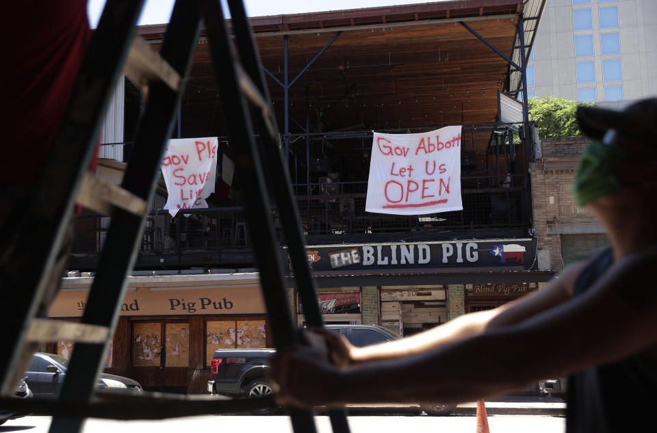 Signs directed at Texas Gov. Greg Abbott are seen behind workers preparing another pub that they hope to reopen soon, in Austin, Texas, Monday, May 18, 2020. Texas continues to go through phases as the state reopens after closing many non-essential businesses to help battle the spread of COVID-19. (AP Photo/Eric Gay)