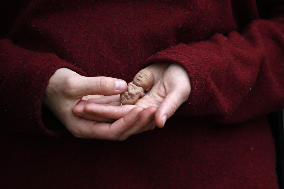 Melanie Wong holds a plastic fetus on Tuesday, April 12, 2022, outside the Hope Clinic for Women in Granite City, Ill. Wong, who opposes abortion, says she was standing outside the clinic to offer support to women seeking abortions who may have a change of heart and need support. Pregnant with her third child, she told her young son, "This is about how big my baby is." (AP Photo/Martha Irvine)