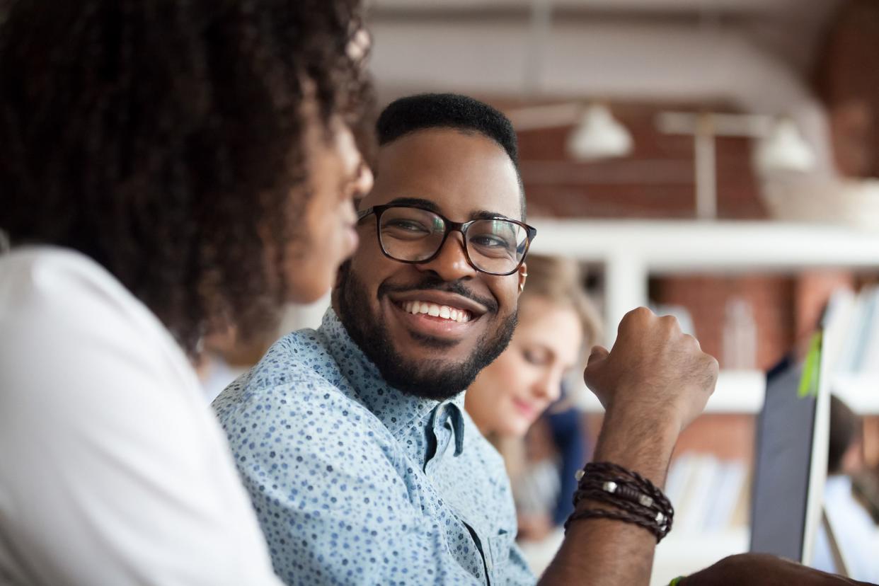 smiling African American male employee look at colleague chatting