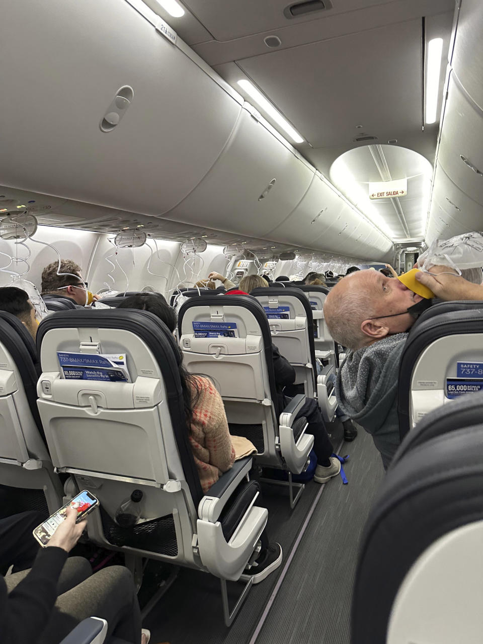 This image provided by Kelly Bartlett shows passengers with oxygen masks on an Alaska Airlines Boeing 737 Max 9, Flight 1282, which was forced to return to Portland International Airport on Friday, Jan. 5, 2024. (Kelly Bartlett via AP)