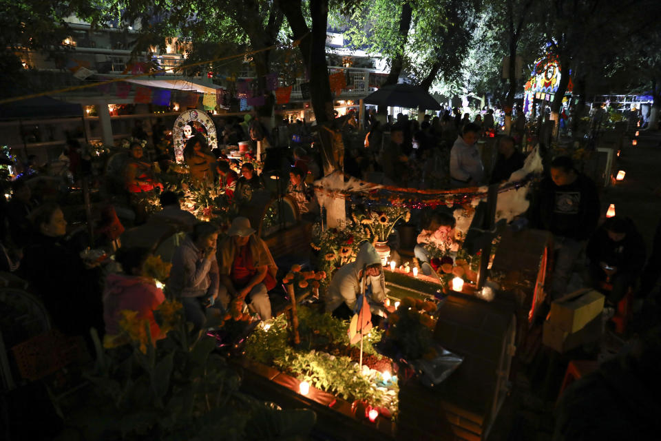 Relatives spend the night next to the tomb of their loved one in the Los Reyes cemetery during Day of the Dead festivities in Mexico City, Friday, Nov. 1, 2019. In a tradition that coincides with All Saints Day and All Souls Day, families decorate the graves of departed relatives with flowers and candles, and spend the night in the cemetery, eating and drinking as they keep company with their deceased loved ones. (AP Photo/Eduardo Verdugo)