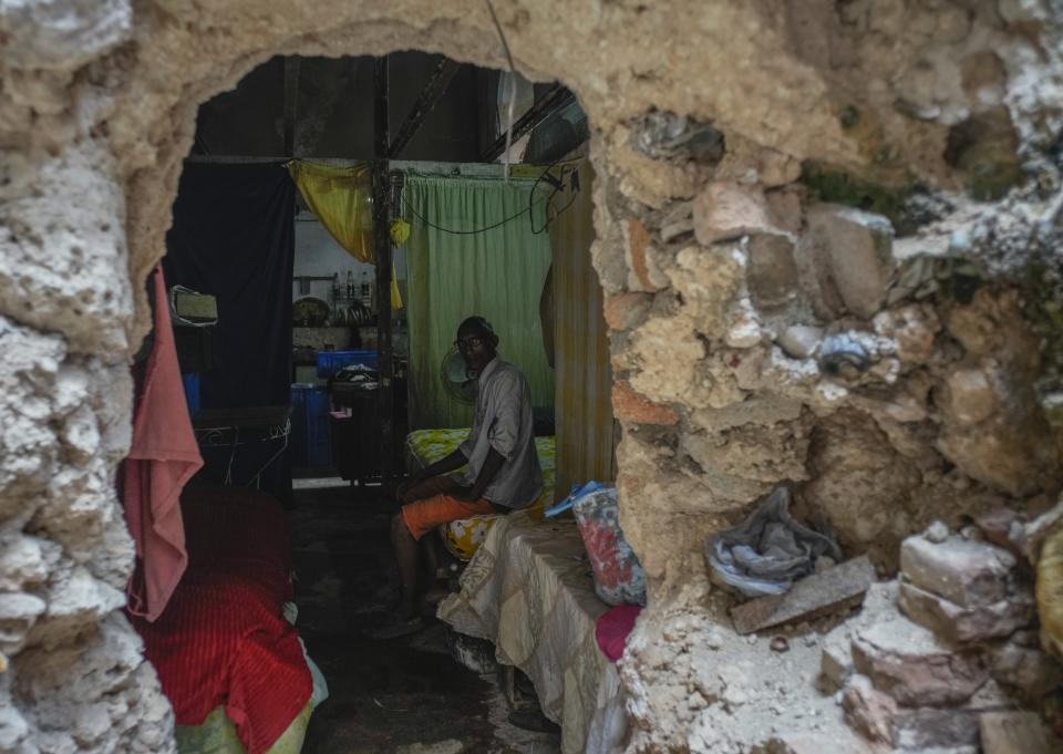 Mario Luis Poll posa sentado para la foto en su cama detrás de una pared quebrada, dentro de una mansión parcialmente derrumbada en la que vive junto a otras familias en la calle Villegas de La Habana, Cuba, el jueves 5 de octubre de 2023. El restaurador de arte de 57 años ha hecho reparaciones para tratar de mantener firme el techo de su estancia, después de que el piso del nivel superior colapsara. (AP Foto/Ramón Espinosa)