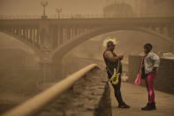 Two people in carnival dress stand beneath a cloud of red dust in Santa Cruz de Tenerife, Spain, Sunday, Feb. 23, 2020. Flights leaving Tenerife have been affected after storms of red sand from Africa's Saharan desert hit the Canary Islands. Saturday's carnival was cancelled but Sunday's events are going ahead. (AP Photo/Andres Gutierrez)