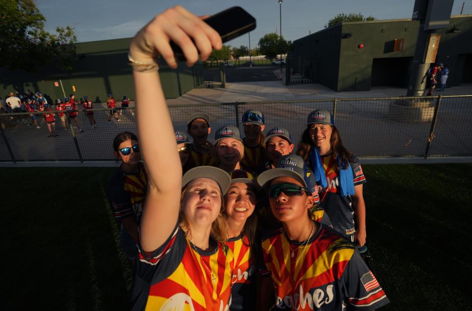 Shelby O’Donnal, 15, front row from left, Keira Izumi, 15, and Angie Valenzuela, 16, gather with their teammates for a selfie during the opening ceremony for Baseball for All, an organization focused on giving girls an opportunity to play baseball, at Hohokam Stadium in Mesa, Ariz. on Wednesday, July 20, 2022.