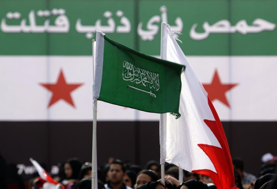 In a photo taken on Feb. 11, 2012, government supporters wave red-and-white Bahraini flags and green Saudi flags at Bahrain's Grand Mosque in Manama, Bahrain. Behind them is a Syrian rebel flag that alters a religious verse to show support for Syrians under siege in the city of Homs. It reads: "Homs, for what sin is she slain?" During a sermon last week at Bahrain's Grand Mosque, the pro-government prayer leader offered sweeping praise to one of the Arab Spring's counter revolutions: Gulf rulers bonding together against dissent with powerful Saudi Arabia as their main guardian. (AP Photo/Hasan Jamali)