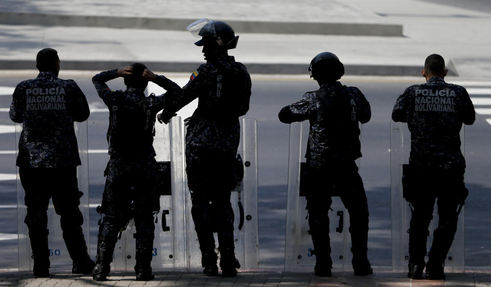 In this Tuesday, March 19, 2019 photo, police stand in anticipation of a march called by a coalition of opposition parties and civic groups who are petitioning lawmakers for a law of guarantees that will protect workers who have been victims of political retaliation and unjustified dismissals, in Caracas, Venezuela. (AP Photo/Natacha Pisarenko)