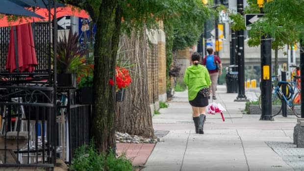 A person wearing rain boots walks down a street with umbrella on July 29, 2021. (Francis Ferland/CBC - image credit)