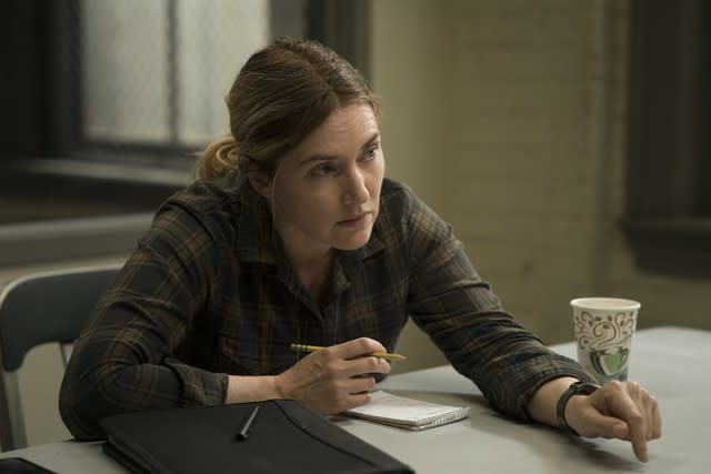 A woman in a flannel shirt sitting at a table with a pencil, notebook and styrofoam cup of coffee