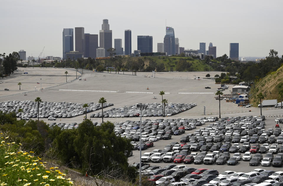 Unused rental cars are stored in the parking lot of Dodger Stadium as downtown Los Angeles is seen in the background, Tuesday, March 31, 2020, in Los Angeles. Dodger Stadium and Angel Stadium are housing the cars as companies are left with a surplus of unused vehicles and limited capacity to store them. The new coronavirus causes mild or moderate symptoms for most people, but for some, especially older adults and people with existing health problems, it can cause more severe illness or death. (AP Photo/Mark J. Terrill)