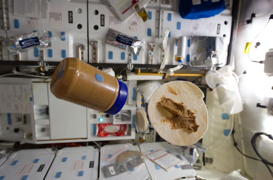 A snack of peanut butter spread on a tortilla and the jar float together during food preparation on space shuttle Discovery's middeck.