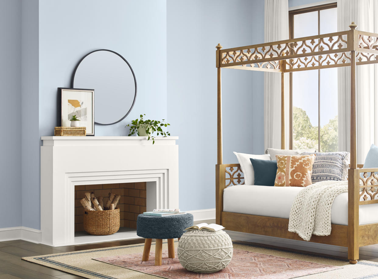  A living room with walls painted a light blue pastel shade with a fireplace and a four poster day bed. 