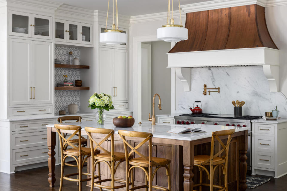 A wood island, brass hardware and copper on the range hood add warmth to an all-white kitchen