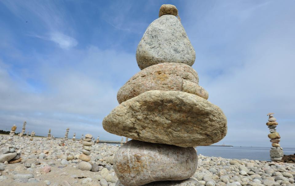 Rock cairns rise up to the sky in Sandwich from a pile of cobble along the beach designed by a patient artist near the east entrance to the Cape Cod Canal taking on the appearance of a modern day Stonehenge.