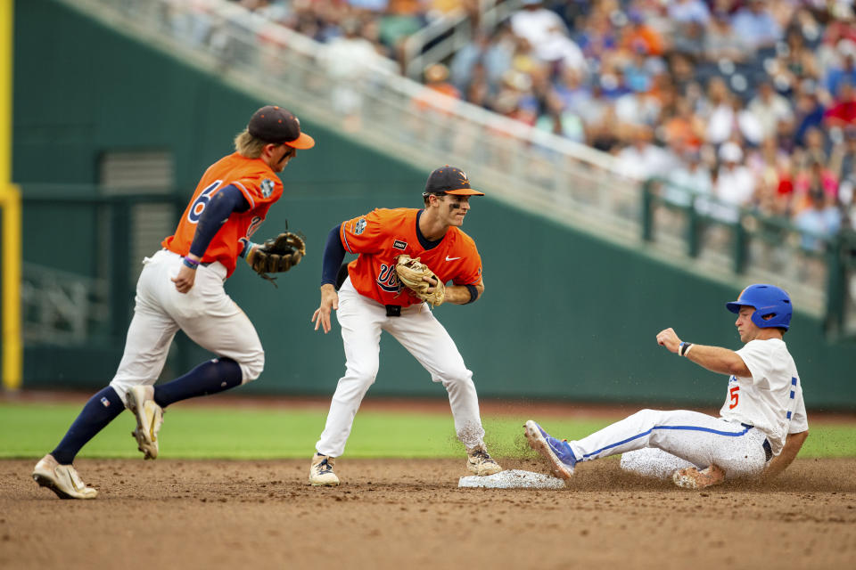 Virginia second baseman Henry Godbout, center, forces out Florida's Colby Halter, right, in the second inning of a baseball game at the NCAA College World Series in Omaha, Neb., Friday, June 16, 2023. (AP Photo/John Peterson)