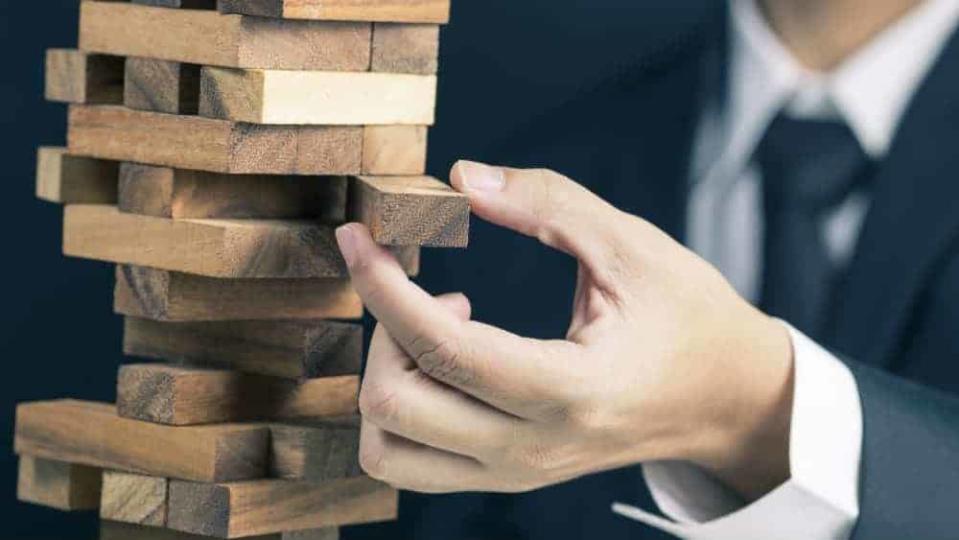 Businessman pulling out wooden brick from toppling stack