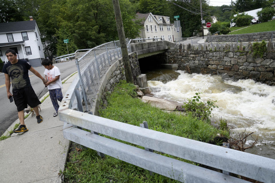 Pedestrians pass a local river whose heavy current flooded nearby Main Street, Monday, July 10, 2023, in Highland Falls, N.Y. Heavy rain has washed out roads and forced evacuations in the Northeast as more downpours were forecast throughout the day. One person in New York's Hudson Valley has drowned as she was trying to leave her home. (AP Photo/John Minchillo)