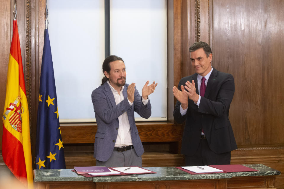 Spain's caretaker Prime Minister Pedro Sanchez, right and Podemos party leader Pablo Iglesias applaud negotiators from both parties after signing an agreement between the two parties in the Spanish parliament in Madrid, Spain, Monday, Dec. 30, 2019. Sanchez hopes to form center-left governing alliance to take office in the country in the coming days. (AP Photo/Paul White)