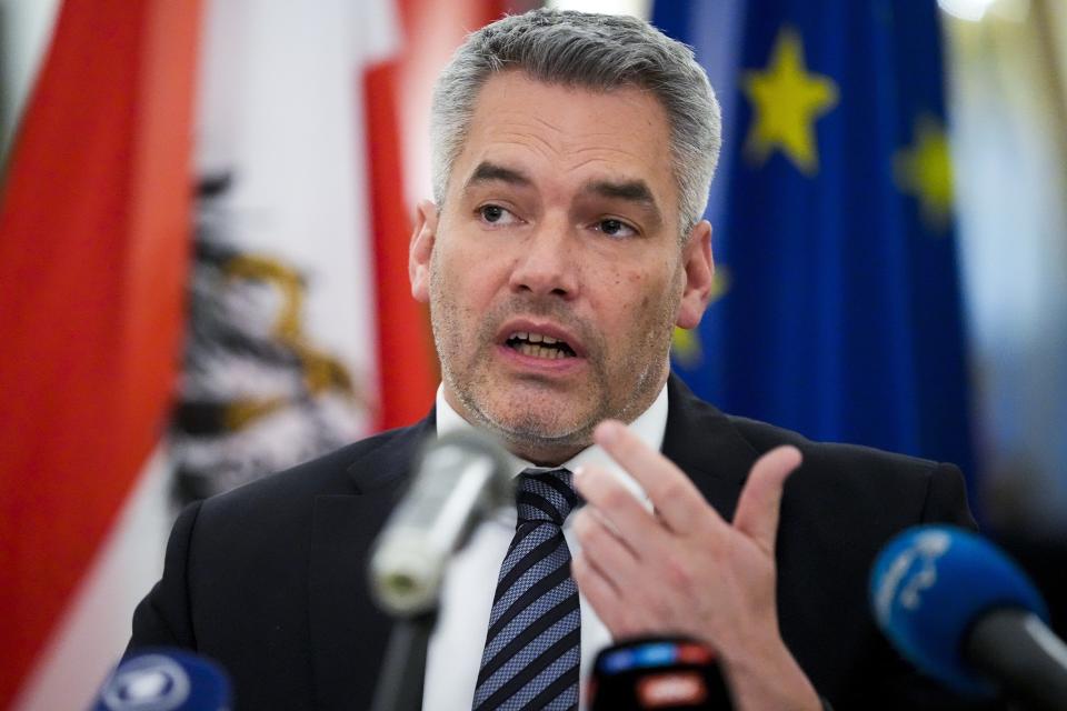 Austria's Chancellor Karl Nehammer gestures while speaking into microphones.