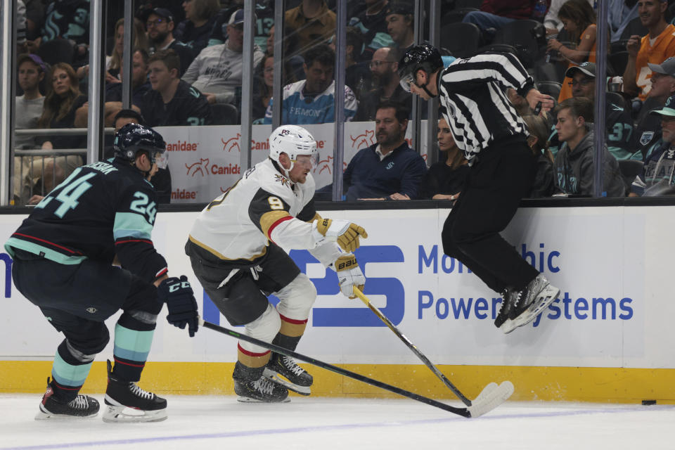 An official jumps out of the way as Seattle Kraken defenseman Jamie Oleksiak (24) and Vegas Golden Knights center Jack Eichel go for the puck during the first period of an NHL hockey game Saturday, Oct. 15, 2022, in Seattle. (AP Photo/Jason Redmond)