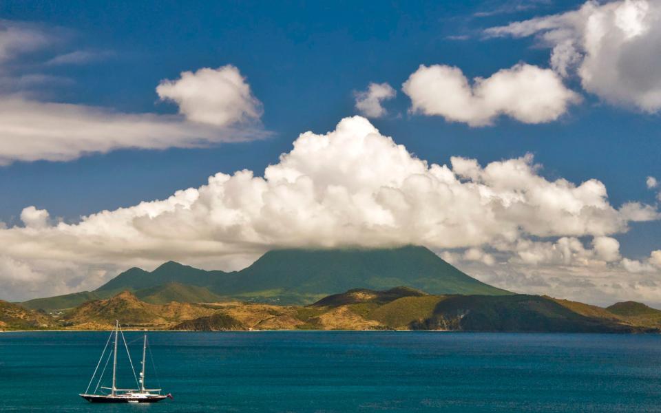 A view of Nevis with a stunning cape as seen from St Kitts with a sailboat passing through the Caribbean Sea in the foreground