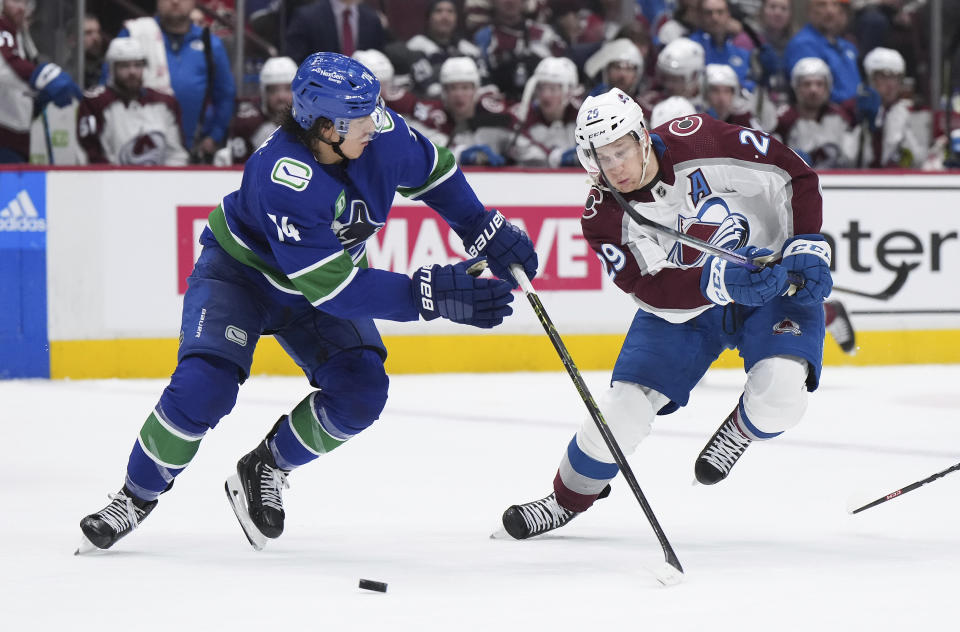 Vancouver Canucks' Ethan Bear, left, and Colorado Avalanche's Nathan MacKinnon vie for the puck during the second period of an NHL hockey game Thursday, Jan. 5, 2023, in Vancouver, British Columbia. (Darryl Dyck/The Canadian Press via AP)