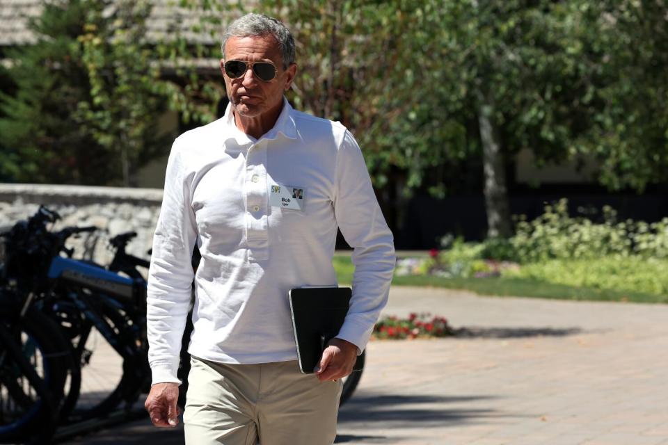 A man in sunglasses walks outdoors, carrying a notebook