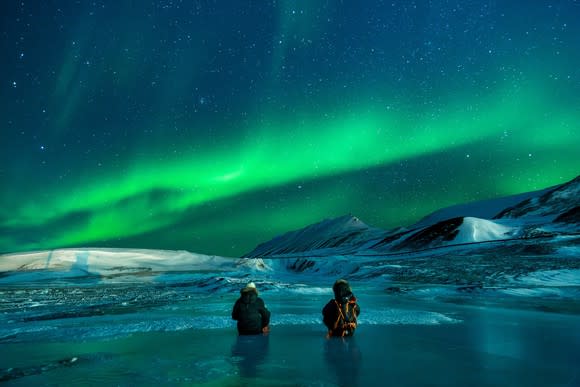 People stand before a stunning display of the aurora borealis in Alaska.