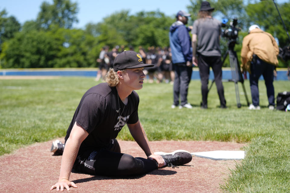 Birmingham-Southern pitcher Trip Barron stretches before practice as a documentary team films at rear, Thursday, May 30, 2024, in Kirtland, Ohio. On Friday, the Panthers will continue an unexpected, uplifting season that has captured hearts across the country by playing in the Division III World Series on the same day the liberal arts college founded on the eve of the Civil War shuts its doors. (AP Photo/Sue Ogrocki)