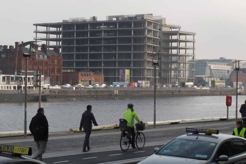 FILE This Thursday, March 22, 2012 file photo shows Irish commuters walking and cycling to their jobs past the abandoned, unfinished headquarters of Anglo Irish Bank in Dublin. Irish police say detectives have arrested the former chief executive of Anglo Irish Bank and charged him over a conspiracy to hide losses at the bank before its 2009 nationalization. Sean FitzPatrick was arrested Tuesday July 24, 2012 at Dublin Airport as he returned from holiday. The 64-year-old FitzPatrick presided over Ireland's runaway property boom, which was swiftly followed by the banking collapse at the heart of the country's 2010 international bailout. Anglo's losses on bad loans to property speculators are nearing €30 billion ($36 billion), or more than Euros 6,500 ($8,000) for every person in Ireland. Ireland's Justice Department says the 3-year probe into fraudulent practices at Anglo is the biggest in the country's criminal history.(AP Photo/Shawn Pogatchnik, File)