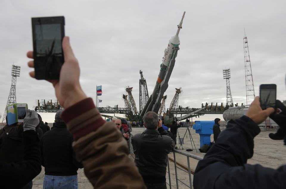 Spectators take pictures of Soyuz TMA-12M spacecraft being lifted to its launch pad at the Baikonur cosmodrome