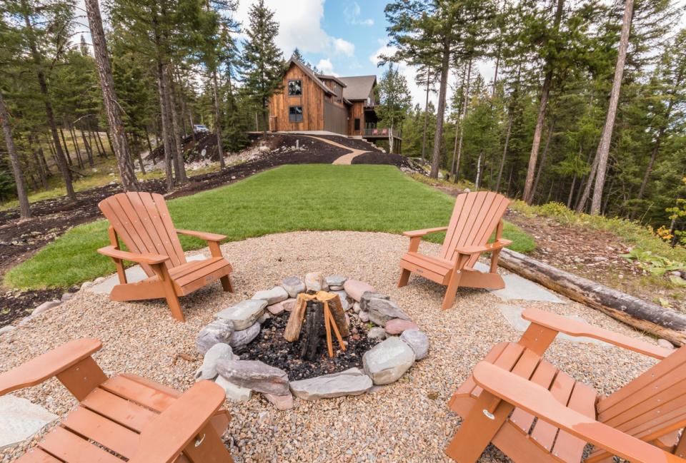 Circular fire pit area with adirondack chairs in back of home in the forest