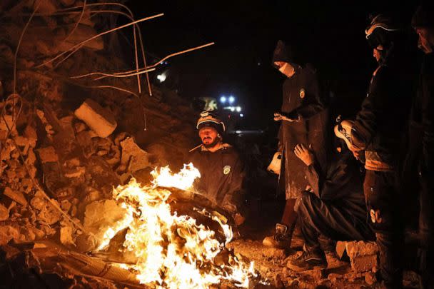 PHOTO: White Helmet Syrian rescue workers warm themselves by a fire next to a collapsed building late on Feb. 6, 2022, in the town of Sarmada, in Syria's rebel-held northwestern Idlib province. (Aaref Watad/AFP via Getty Images)