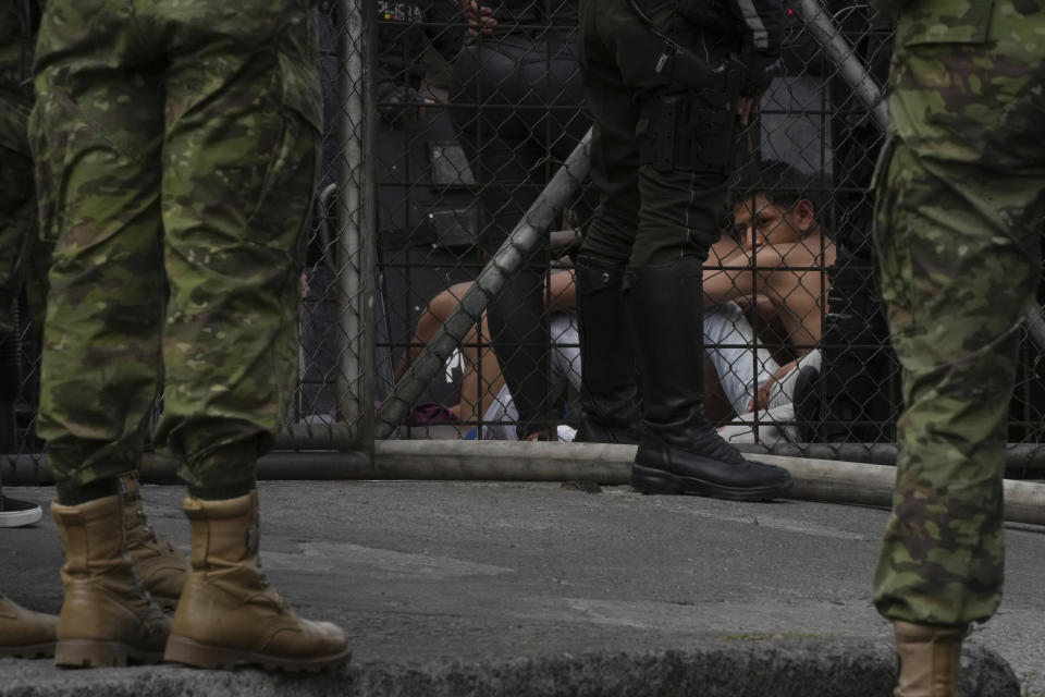 A juvenile looks out from behind a guarded area of the Virgilio Guerrero detention center after inmates were evacuated to a patio due to a fire at the center set by a group of detainees, in Quito, Ecuador, Thursday, Aug. 31, 2023. (AP Photo/Dolores Ochoa)